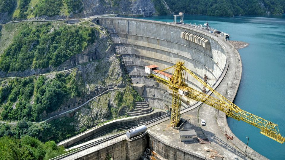 A dam under construction, with a tower crane working beside the spillway
