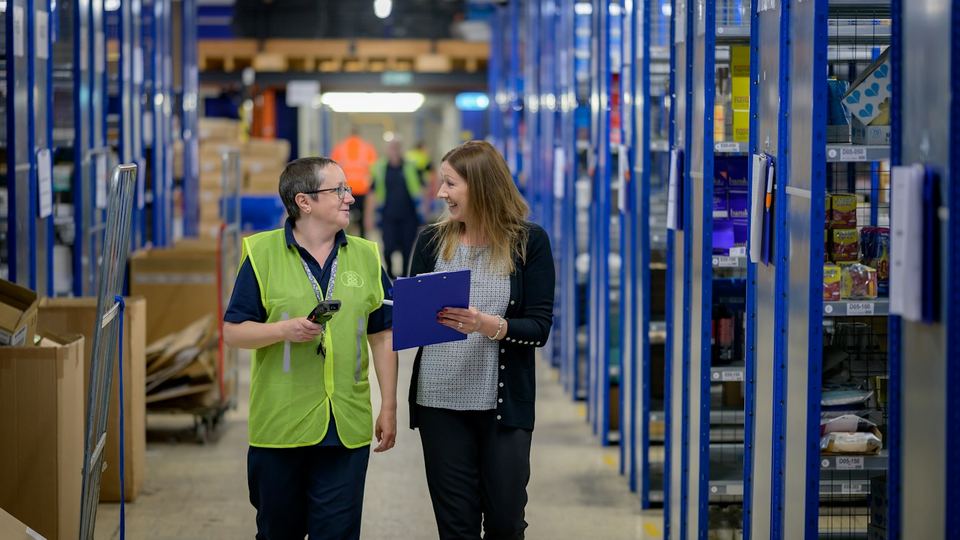 Two warehouse staff walking an aisle of racked stock with a clipboard
